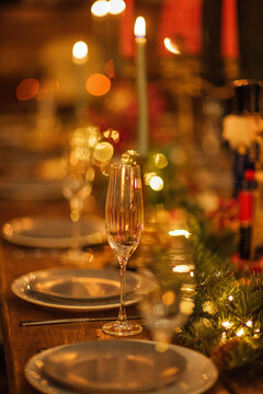 Elegant dining table set for a festive celebration with sparkling glassware, decorative plates, and candles, surrounded by greenery and warm ambient lighting