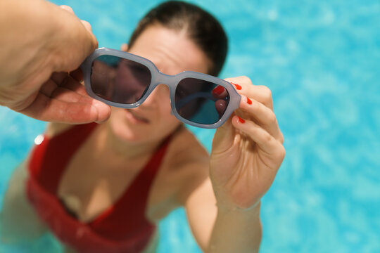 Woman in a pool reaching for sunglasses on a sunny day