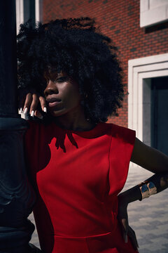 Elegant Black Woman in Red Dress Standing in Dramatic Sunlight