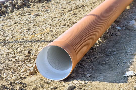 Long drainage PVC pipe rests on ground at construction site with loose gravel nearby.