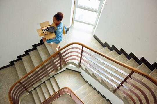 Woman carries a box of things down the stairs