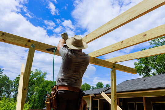 Carpenter uses pneumatic nail gun to attach wooden beams in construction project at house