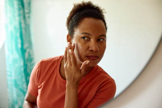 Woman applies face cream in front of a mirror