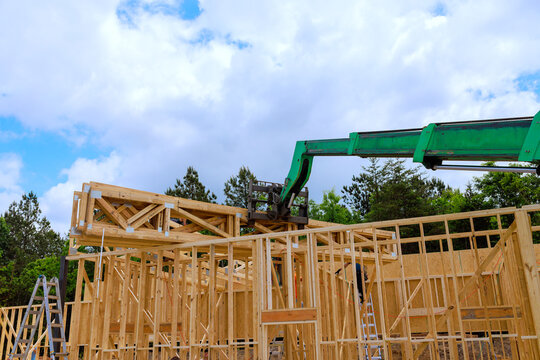 Workers use crane to lift wooden structures for building under construction in wooded area