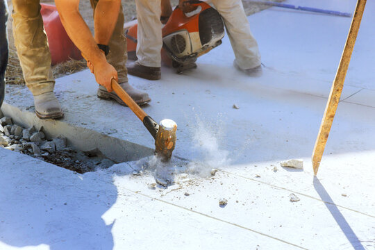 Workers are using tools to break concrete at construction site dust rises as they work hard.