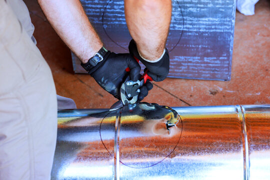Builder is cutting round hole in HVAC metal pipe using tool during metal duct assembly