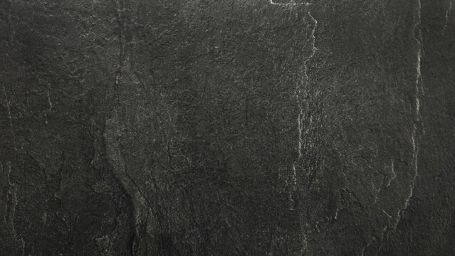 Dark black natural stone surface with subtle cracks, rough texture and weathered details. Abstract slate background with a dramatic charcoal gray pattern.