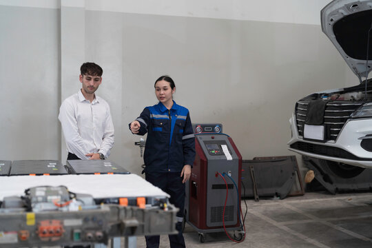 Electric vehicle car auto services. EV garage. Diagnostic battery pack. Customer and mechanic discussion and diagnosing electric car vehicles battery, component checks at auto workshop