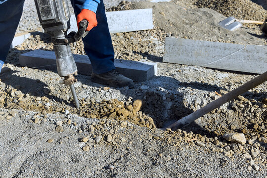 Contractor operates jackhammer on construction site gravel dirt surround work area.