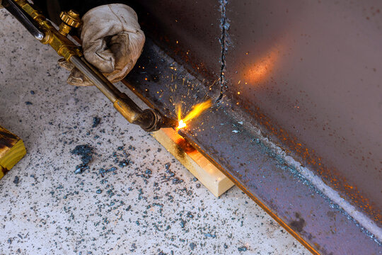 Worker is welding metal pieces together in workshop sparks are flying as torch ignites metal.