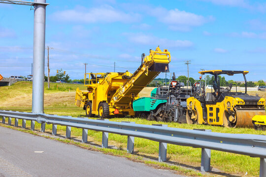 Large machines are operating on grass beside road during daytime with clear weather.