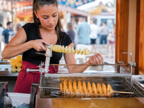 Spiralkartoffel am Spie&szlig; &ndash; Verk&auml;uferin schneidet eine Kartoffelspirale und bereitet sie im hei&szlig;en Fett zu. Beliebtes Street Food auf dem Volksfest mit frischer Zubereitung.