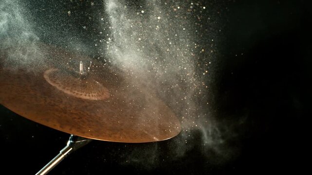 Super slow motion footage at 1000 fps of golden glitter and white powder flying above a vibrating cymbal, capturing sparkling particles, dust, metallic movement, and dynamic energy.