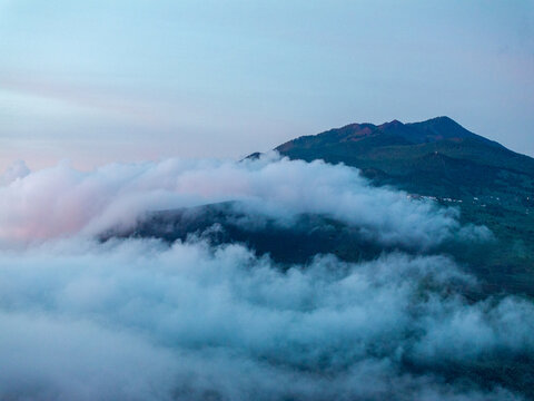 Aerial view of La Palma mountains partially obscured by a thick layer of clouds under a soft morning sky in the Canary Islands, Spain.