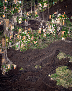 Aerial view of La Palma, showing volcanic lava flows encroaching on residential areas with houses and roads, Canary Islands, Spain.