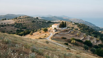 Obraz premium Wide panoramic view of a hilly countryside with a white house and winding road coastally situated