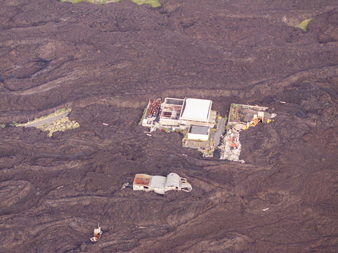 Aerial view of La Palma volcanic landscape featuring solidified lava flows surrounding partially buried industrial buildings and structures Canary Islands, Spain.