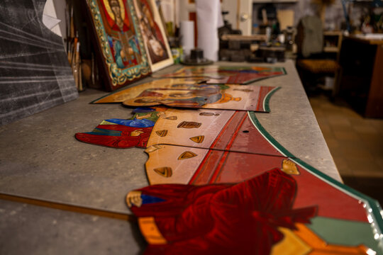 Orthodox painted icon fragments placed on workbench in art restoration workshop, depicting biblical scenes for church iconostasis manufacturing and preservation.