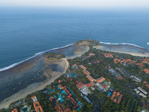 Aerial view of Nusa Dua Resort Area Road surrounded by lush greenery, red-tiled hotel roofs, and sandy beaches along the coastline in Kecamatan Kuta Selatan, Bali, Indonesia.