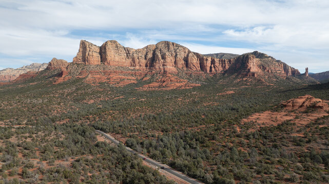 Aerial view of the iconic red rock mountains and desert landscape with a winding road under a clear sky in Sedona, Arizona, United States.