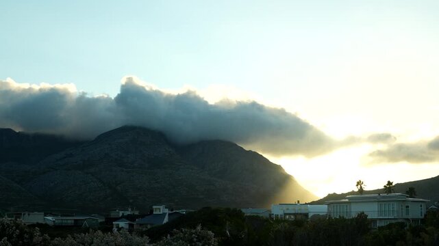 Low clouds rolling across dark mountain peaks as golden sunrise light appears on the horizon, creating a dramatic morning landscape with atmospheric changing weather