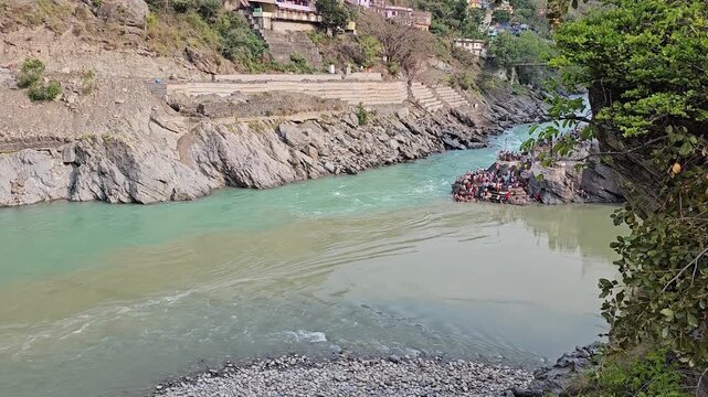 Scenic view of a river confluence in a mountainous landscape, with contrasting blue-green and sediment-rich water flowing between rocky banks. 