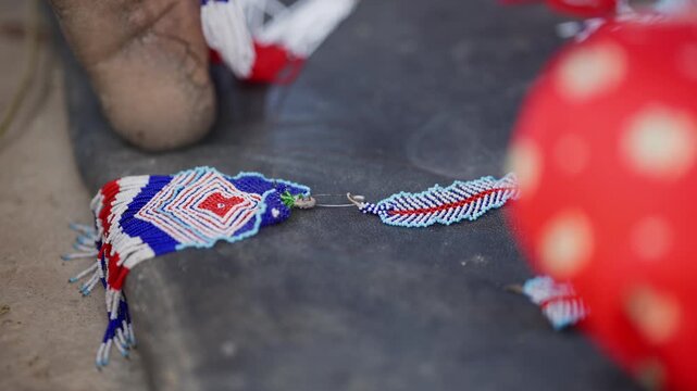 Macro close up of finished red white and blue pote glass bead pendant with fringe tassels resting on stone ground in Nepali village