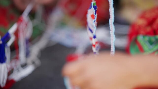 Close up hand with red bangle holding twisted blue pote bead thread against vivid red traditional fabric in far west Nepali setting