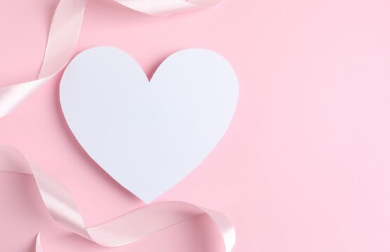 White paper heart with pink satin ribbon on pastel background, space for text