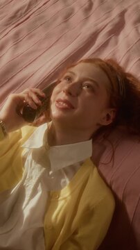 Vertical shot of Caucasian teenager lying on bed and talking on retro telephone. Clip is ideal for youth lifestyle commercials, nostalgic brand campaigns or telecommunication advertisements