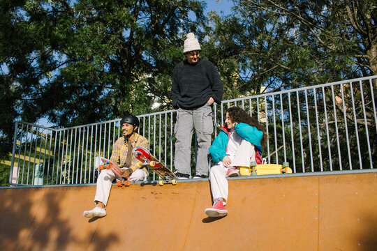 Gen-z friends relax with skateboards at sunny skatepark
