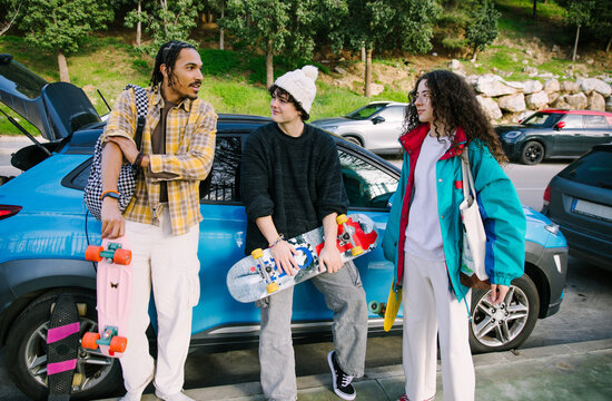 Gen Z friends with skateboards beside blue car outdoors