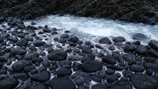 Ocean waves crashing over black volcanic rocks on the shoreline in this natural motion.