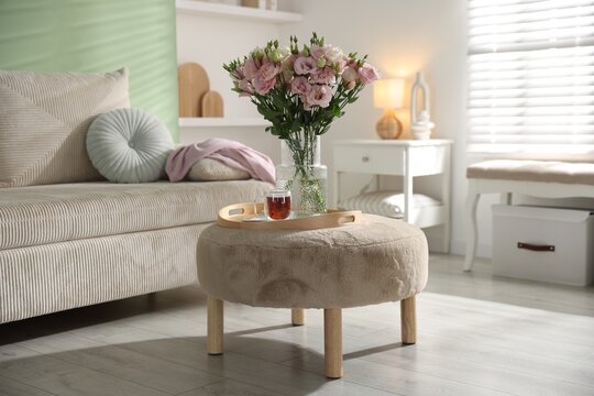 Bouquet of beautiful eustoma flowers in vase and cup of tea on pouf indoors