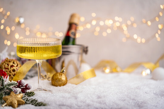 Elegant coupe glass filled with bubbly champagne sits on snow with a bottle, golden ribbon, and soft Christmas lights in a celebratory winter scene. Ideal for holiday greeting cards,