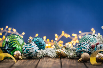 Naklejka premium A Christmas background featuring navy and teal ornaments wrapped with gold ribbon on rustic wood, framed symmetrically against a deep blue backdrop with twinkling lights and copy space.