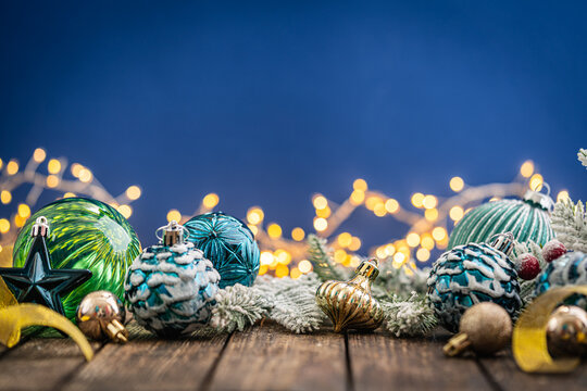 A Christmas background featuring navy and teal ornaments wrapped with gold ribbon on rustic wood, framed symmetrically against a deep blue backdrop with twinkling lights and copy space.