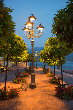 Nighttime scene on the Gargnano waterfront promenade; lit streetlamps and orange trees.
