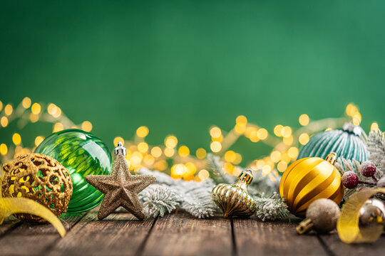 A Christmas background featuring gold and emerald ornaments, a glittering star, and frosted pine on rustic wood, set against a rich green backdrop with twinkling lights and copy space.