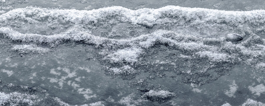 Ice texture covered with snow on frozen surface in winter close-up
