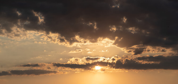 Sun setting through dark clouds in evening sky