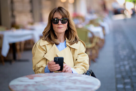Stylish mature woman sitting in a classic European cafe and using her smartphone