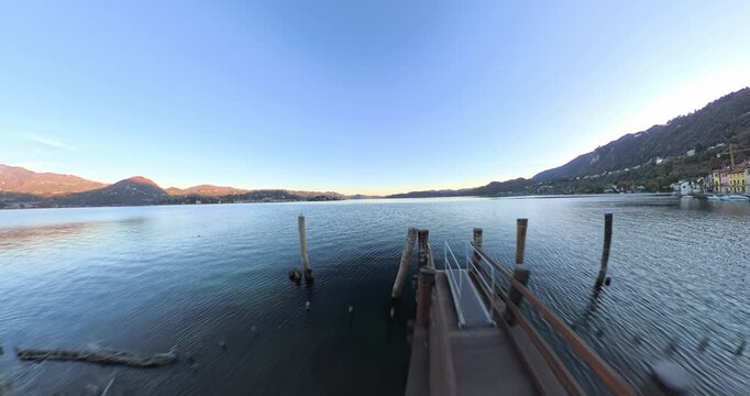 Drone flying under metal archway gate at boat pier in Pella along Lake Orta at sunset in Piedmont, Italy