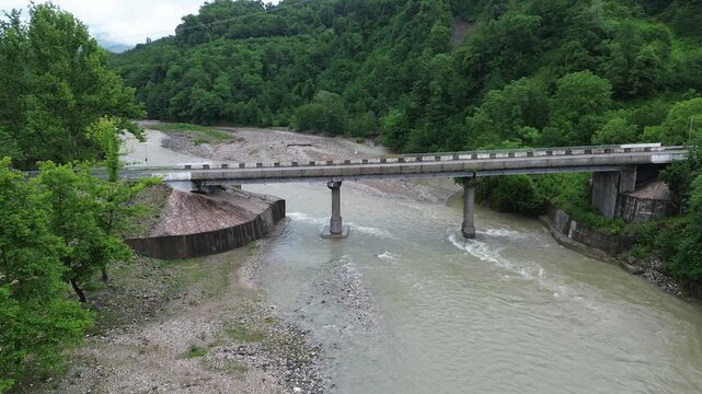 Static drone shot hovering in front of a concrete road bridge crossing the Tekhuri river near Martvili, Georgia, dense green vegetation covering both riverbanks. Overcast morning after rain.