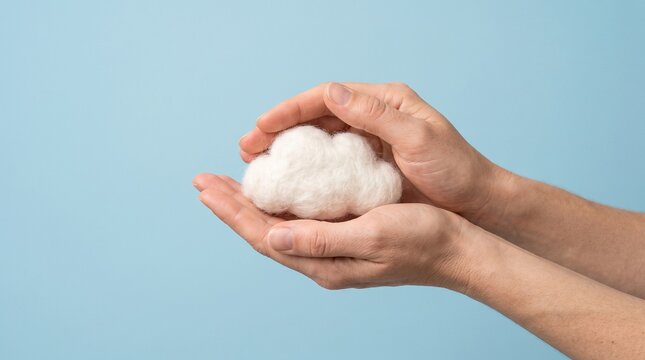 Human hands gently cupping a soft white cotton cloud against a minimal blue backdrop. Symbolizes protection and data storage. Perfect for cloud computing and tech services.