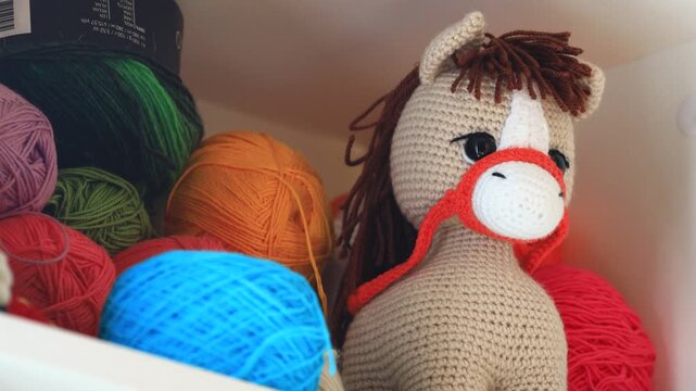 A colorful crocheted stuffed horse surrounded by yarn balls and threads