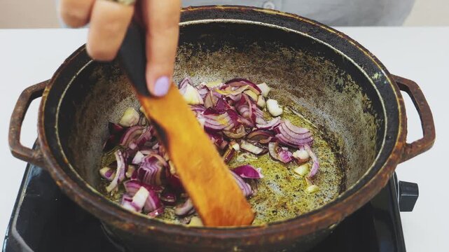 Sliced red onions are fried in vegetable oil in a deep cast-iron skillet
