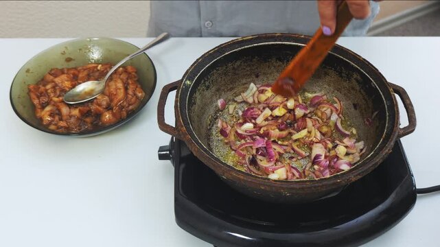 Onions are fried in vegetable oil in a deep cast-iron skillet and stirred