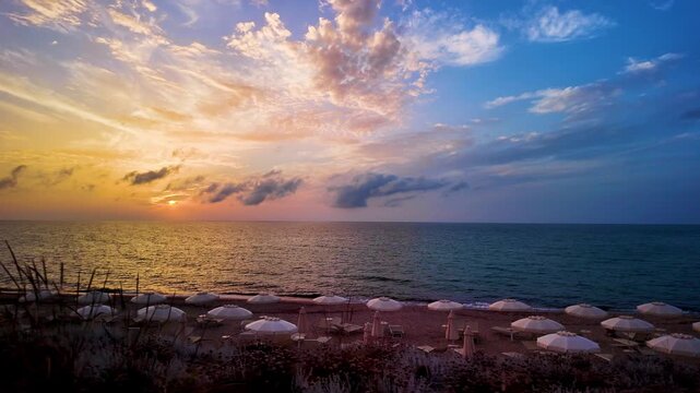 Golden sunset over the sea horizon on an empty sandy beach with umbrellas