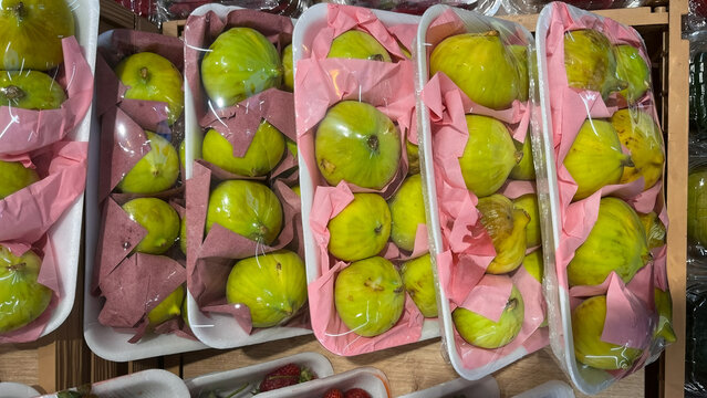 An arrangement of fresh green figs wrapped in pink paper and packaged on foam trays.